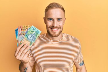 Avustralyalı genç beyaz adam elinde dolarlar tutuyordu. Pozitif ve mutlu görünüyordu. Ve gülümsüyordu. 