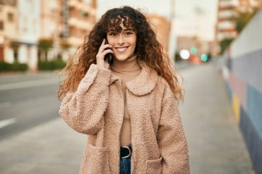 Genç İspanyol kadın gülümsüyor. Şehirdeki akıllı telefondan konuşuyor.