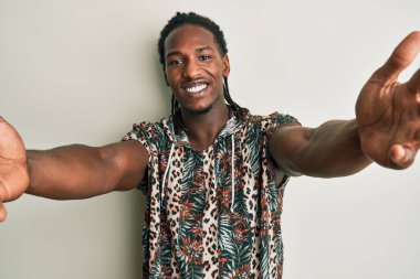 Moda tişörtü giymiş Afro-Amerikan bir adam kameraya sarılmak için gülümseyerek bakıyor. Mutluluğu kucaklayan neşeli bir ifade.. 