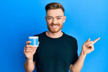 Kulak kiri temizleyici tutan genç kızıl saçlı adam gülümsüyor. 