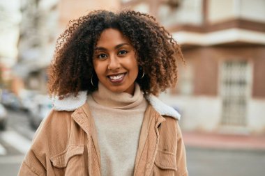 Genç Afrikalı Amerikalı kadın gülümseyerek şehirde mutlu mesut duruyor..