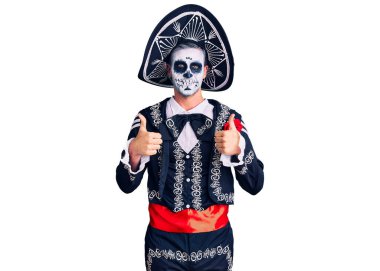 Arka plan başarı işareti üzerine ölü kostümün giyildiği gün elinde olumlu bir jest yapan, gülümseyen ve mutlu genç bir adam. Neşeli ifade ve kazanan jest. 