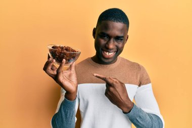 Genç Afrikalı Amerikalı adam elinde kuru üzümlü bir kaseyle mutlu mesut elini ve parmağını gösterdi. 