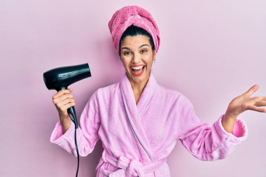 Genç İspanyol kadın duş bornozu giyiyor kurutucu kullanıyor başarıyı mutlu bir gülümsemeyle kutluyor ve kazanan el kaldırarak ifade ediyor 