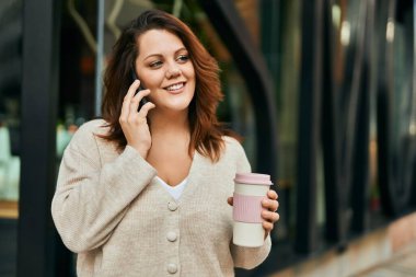 Genç İrlandalı artı cüsseli kız akıllı telefonla konuşuyor ve şehirde kahve içiyor..