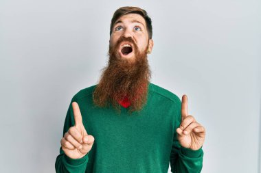 Uzun sakallı, sıradan giyinen kızıl saçlı adam şaşkın şaşkın yukarı bakıyor, parmaklarıyla işaret ediyor ve kollarını kaldırıyordu.. 