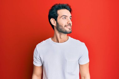 Gündelik beyaz tişört giyen genç İspanyol adam yüzünde gülümseme ve doğal ifadeyle yan yana bakıyor. Kendinden emin gülen. 