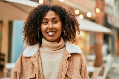 Genç Afrikalı Amerikalı kadın gülümseyerek şehirde mutlu mesut duruyor..