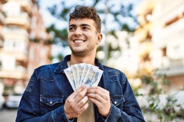 Genç İspanyol gülümseyen adam, şehirde Peru sol banknotlarını tutarken mutlu.