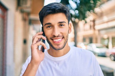 Genç Latin adam gülümsüyor ve şehirde akıllı telefondan konuşuyor..