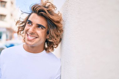 Genç yakışıklı İspanyol gülümseyen mutlu bir adam şehrin duvarına yaslanıyor.