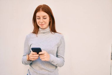 Genç İrlandalı kız şehirde akıllı telefon kullanarak mutlu bir şekilde gülümsüyor..