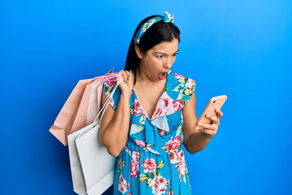 Jonge Latijnse Vrouw Met Boodschappentassen Smartphone Bang Geschokt Met Verbazing — Stockfoto