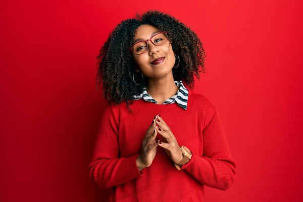 Beautiful african american woman with afro hair wearing sweater and glasses hands together and fingers crossed smiling relaxed and cheerful. success and optimistic