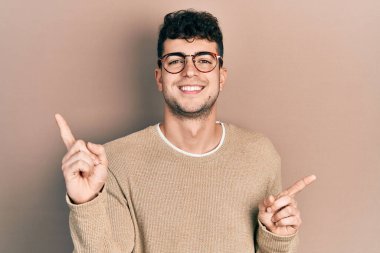 Gündelik kıyafetler ve gözlük takan genç İspanyol adam farklı yönleri gösteren kendine güvenle gülümsüyor. reklam için kopyalama alanı 