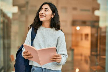 Genç ortadoğu öğrencisi kız şehirde mutlu bir şekilde kitap okuyor..