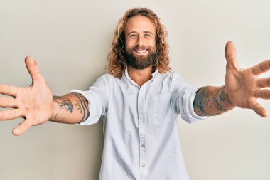 Sakallı, uzun saçlı, sıradan beyaz gömlekli yakışıklı kameraya sarılıp gülümseyen bir adam. Mutluluğu kucaklayan neşeli bir ifade.. 