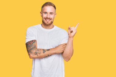 Genç İrlandalı sıradan kıyafetler giyen, yüzünde kocaman bir gülümseme olan, eli ve parmağı kameraya bakan genç bir adam.. 