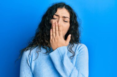 Kıvırcık saçlı, günlük kıyafetler giyen genç esmer kadın ağzıyla esnemekten sıkılmış. Huzursuz ve uykulu.. 