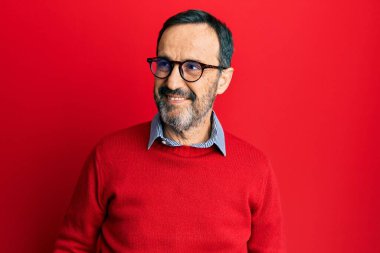 Orta yaşlı İspanyol bir adam, günlük kıyafetler ve gözlük takıyor. Yüzünde gülümsemeyle yan yana bakıyor, doğal bir ifade. Kendinden emin gülen. 