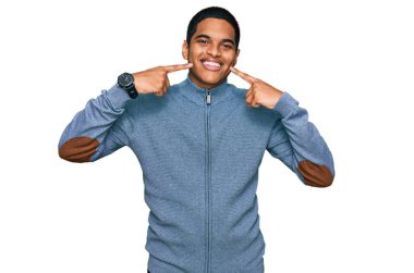 Gündelik kazak giyen, neşeli gülümseyen ve parmaklarıyla ve ağzıyla işaret eden genç, yakışıklı İspanyol bir adam. diş sağlığı kavramı. 