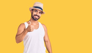Gündelik yaz şapkası takan İspanyol genç adam elleriyle mutlu bir jest yapıyor. Kameraya bakıp başarıyı gösteren ifade. 
