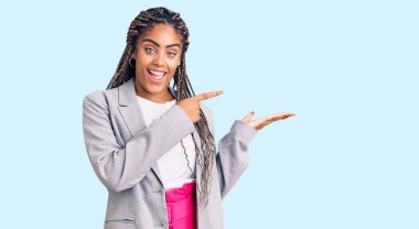 Saçları örgülü genç Afro-Amerikalı kadın kameraya hayret ediyor ve gülümsüyor.. 