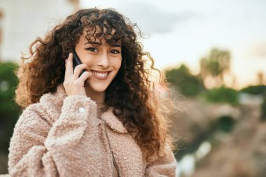 Genç İspanyol kadın gülümsüyor. Şehirdeki akıllı telefondan konuşuyor.