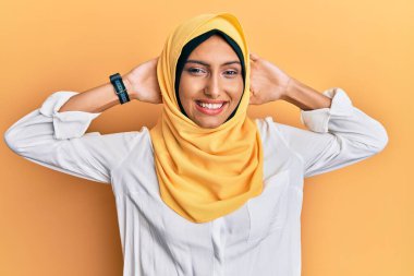 Genç esmer Arap kadın geleneksel İslami başörtüsü takıyor rahatlıyor ve esniyor, kolları ve elleri başının ve boynunun arkasında mutlu bir şekilde gülümsüyor. 