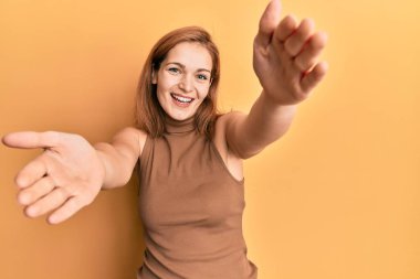 Kolsuz elbiseli, sıradan giyinmiş, kolları açık kameraya bakıp sarılmak için gülümseyen beyaz bir kadın. Mutluluğu kucaklayan neşeli bir ifade.. 