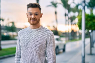 Genç beyaz adam gülümseyerek şehirde mutlu mesut duruyor..