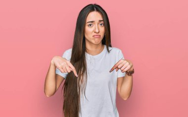 Gündelik beyaz tişört giyen genç İspanyol kız üzgün ve üzgün görünüyor, parmaklarıyla yönü gösteriyor, mutsuz ve depresif.. 