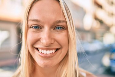 Genç sarışın kız gülümseyerek şehirde mutlu mesut yürüyor..