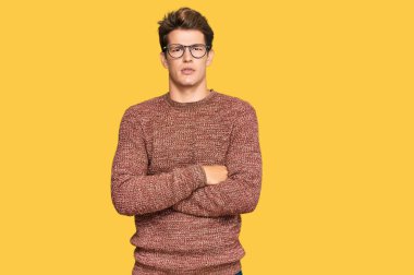 Sıradan süveter giyen, gözlüklü, kuşkucu ve gergin, yüzünde çapraz kollu tasvip etmeyen yakışıklı beyaz bir adam. negatif kişi. 