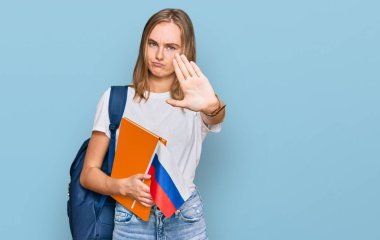 Güzel sarışın değişim öğrencisi. Elinde Rus bayrağı var. Dur işareti yapıyor. Ciddi ve kendinden emin bir ifadeyle. 
