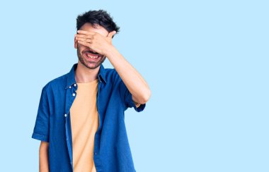 Gündelik kıyafetler giyen, gülümseyen ve gülümseyen genç İspanyol adam şaşırmak için gözlerini kapatıyor. kör kavram. 