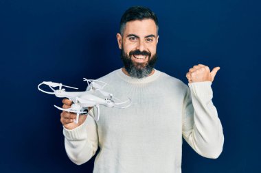 Genç İspanyol bir adam İHA 'yı elinde tutuyor başparmağıyla yan tarafa bakıyor mutlu bir şekilde ağzı açık gülümsüyor. 