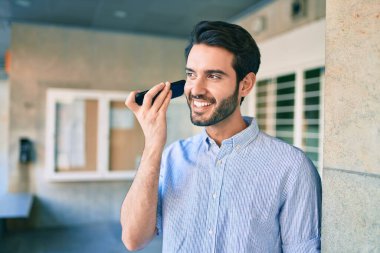 Genç İspanyol adam gülümsüyor. Şehirdeki akıllı telefonu kullanarak mutlu bir sesli mesaj dinliyor..