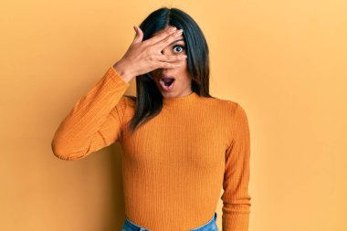 Genç Latin transseksüel kadın gündelik kıyafetler giyiyor. Şokta, yüzünü ve gözlerini eliyle kapatıyor. Parmaklarından bakıyor. 