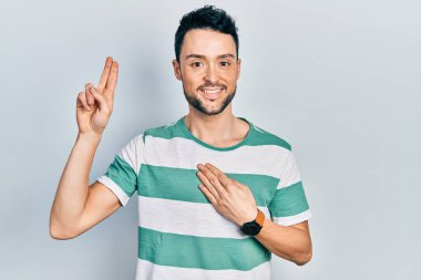 Gündelik kıyafetler giyen genç İspanyol adam gülümsüyor. Göğsü ve parmakları havada küfür ediyor. Sadakat yemini ediyor. 