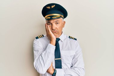 Yakışıklı, orta yaşlı, uçak pilotu üniforması giyen, yorgun ve bunalımda kollarını kavuşturmaktan sıkılmış görünen olgun bir adam.. 