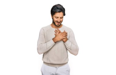 Gündelik kıyafetler giyen genç İspanyol adam elleri göğsünde, gözleri kapalı ve yüzünde minnet dolu bir jest ile gülümsüyor. sağlık kavramı. 