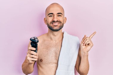 Tıraş bıçağı tutan kel genç adam gülümsüyor mutlu bir şekilde elini ve parmağını yana doğru gösteriyor. 