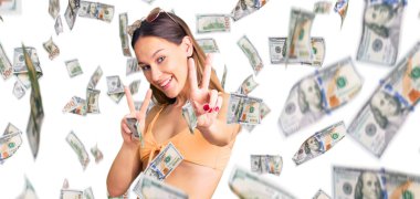 Güzel esmer, bikini giyen, güneş gözlüklü, gülümseyen ve parmaklarını zafer işareti yaparken gösteren genç bir kadın. İki numara..