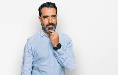 Orta yaşlı, sakallı, iş gömleği giyen, kameraya kendinden emin kollarını kavuşturup gülümseyen ve çenesini kaldırmış bir adam. Olumlu düşünmek. 