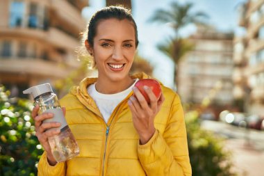 Genç İspanyol kız şehirde bir şişe su içip elma yiyor..