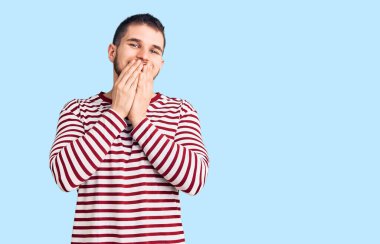 Çizgili süveter giyen genç yakışıklı adam gülüyor ve utanıyor kıkır kıkır kıkır kıkır gülüyor eller, dedikodu ve skandal konsepti ile ağzını kapatıyor 