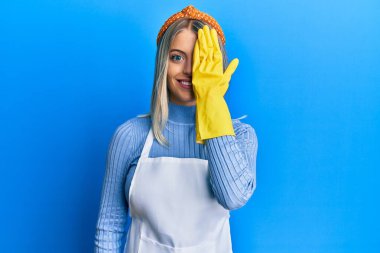 Güzel sarışın kadın temiz önlük giyiyor ve eldivenlerle bir gözünü eliyle kapatıyor, yüzünde kendine güvenen bir gülümseme ve sürpriz bir duygu var.. 