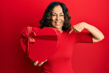 Orta yaşlı İspanyol kadın sevgililer günü hediyesini tutarken mutlu ve gururlu bir gülümsemeyi işaret ediyor. 