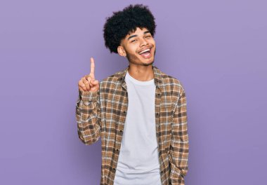 Afro saçlı, genç Afro-Amerikan bir numaralı parmağını gösterip, gülümseyerek mutlu ve kendinden emin bir şekilde gülümsedi.. 